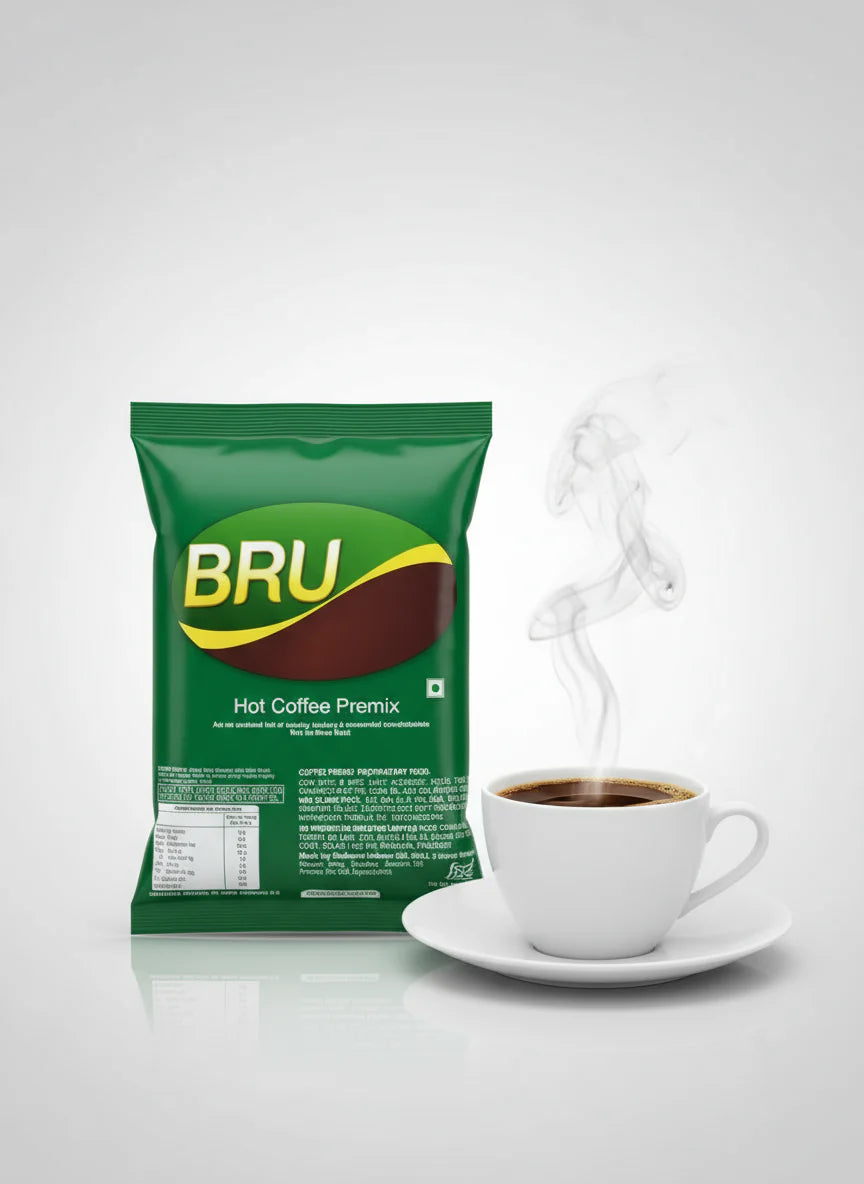 Bru coffee premix 1kg green packet beside a steaming cup of coffee on a white saucer