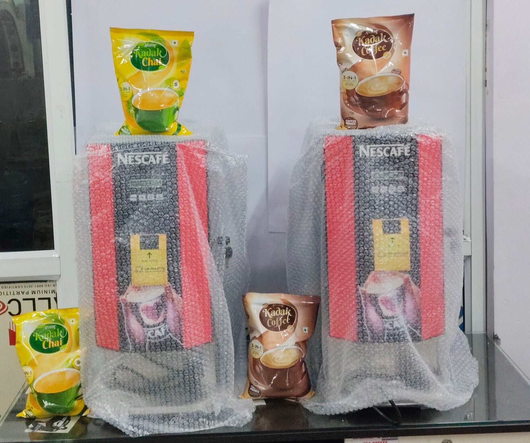 Two Nescafe 2-lane office coffee machines wrapped in bubble wrap with coffee packets on top
